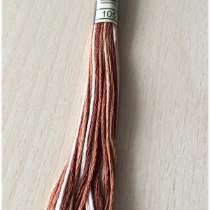May include: A skein of embroidery floss in shades of brown, white, and beige. The floss is labeled with the number "105".