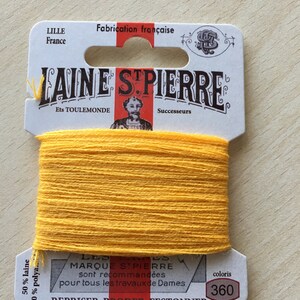 May include: A spool of yellow embroidery floss labeled "Laine St. Pierre" with the text "Ets Toulemonde Successeurs" and "50% laine 50% polya." The label also includes the text "Marqué St. Pierre sont recommandées pour tous les travaux de Dames" and "Repriser Broder Festonner." The color number is 360.