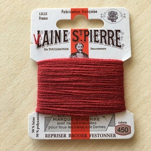 Könnte beinhalten: Eine Spule roten Stickgarns mit der Aufschrift "Laine St. Pierre" und dem Text "50% laine 50% polyamide" und "coloris 450".