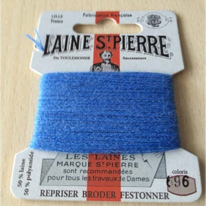 May include: A spool of blue embroidery floss with a white label that reads "LAINE STPIERRE" and "LES LAINES MARQUE STPIERRE sont recommandées pour tous les travaux de Dames REPRISER BRODER FESTONNER" with the color number "696".