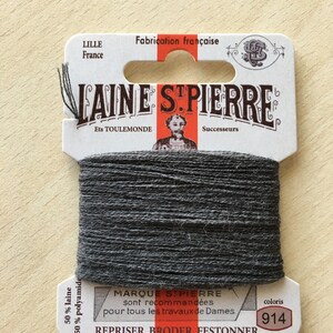 May include: A spool of dark gray Laine St. Pierre thread, with a label that reads "Fabrication française" and "LILLE France." The label also includes the text "REPRISER BRODER FESTONNER" and the color code "914."