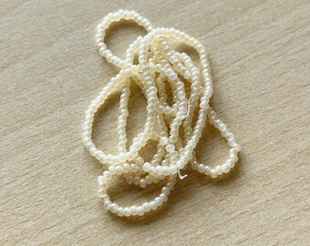 May include: A pile of off-white seed beads, a type of craft supply used for jewelry making.