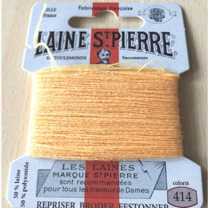 May include: A spool of orange embroidery floss with the text "LAINE STPIERRE" and "LES LAINES MARQUE STPIERRE" on the label. The label also includes the text "coloris 414" and "REPRISER BRODER FESTONNER".