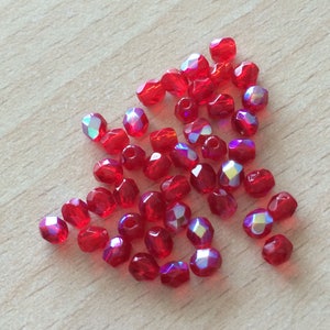 May include: A group of red iridescent glass beads. The beads are faceted and have a shiny finish.