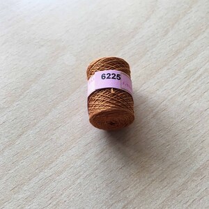 Può includere: Un rocchetto di filo marrone con un'etichetta rosa su cui è scritto "6225".