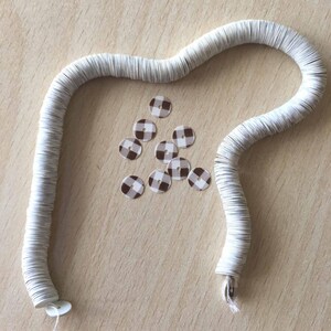 May include: A white coil of paper circles with a pile of brown and white gingham patterned sequins.