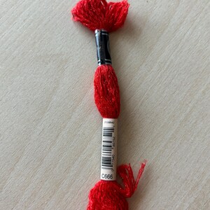 May include: A skein of red embroidery floss with a silver sparkle. The floss is wrapped around a white label with the number C666 printed on it.