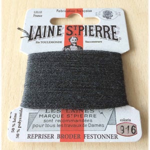 May include: A spool of dark gray embroidery floss with a white label that reads "LAINE STPIERRE" and "LES LAINES MARQUE STPIERRE sont recommandées pour tous les travaux de Dames REPRISER BRODER FESTONNER" with the color number "916".