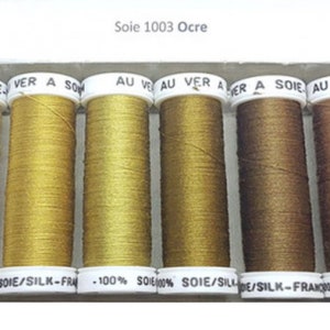 May include: Six spools of thread in various shades of brown and gold. The spools are labelled "Soie 1003 Ocre" and "Soie/Silk-France".