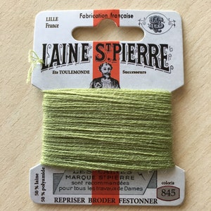 May include: A spool of green embroidery floss labeled "Laine St. Pierre" with the text "Les Fils Marque St. Pierre sont recommandées pour tous les travaux de Dames" and "Repriser Broder Festonner". The spool is labeled with the color number "845".