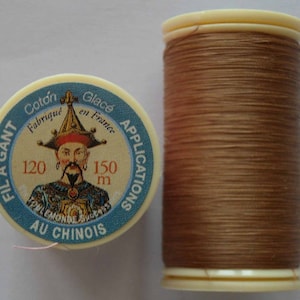 Peut inclure: Une bobine de fil brun avec une étiquette qui indique "FIL A GANT Coton Glacé Fabriqué en France APPLICATIONS AU CHINOIS 120 150 m".