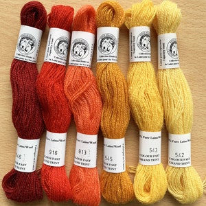 Op de afbeelding: Zes klosjes borduurgaren in tinten rood, oranje en geel. De klosjes zijn gelabeld met de merknaam "Fine Dauphinoise", het kleurnummer en de woorden "Pure Laine/Wool" en "Colour Fast Grand Teint".