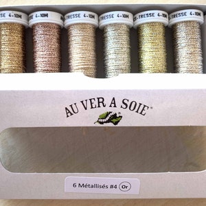 Op de afbeelding: Een doos met zes metalen borduurgaren in goud, ros&eacute; goud en zilver tinten. De doos is gelabeld "AU VER A SOIE" en "6 M&eacute;tallis&eacute;s #4 Or".