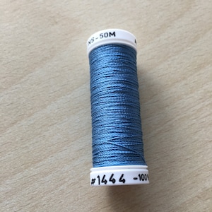 Peut inclure: Une bobine de fil bleu avec une étiquette blanche indiquant "NS-50M #1664 -100".