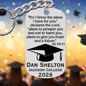 May include: A silver keychain with a graduation cap design. The keychain has the text "For I know the plans I have for you," declares the Lord, "plans to prosper you and not to harm you, plans to give you hope and a future." Jer 29:11. It also includes the name "Dan Shelton", "Jackson College", and the year "2026".