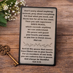 May include: A rectangular plaque with a black border and engraved text. The text includes religious verses and phrases about peace and faith. A decorative key and white flowers are also in the image.