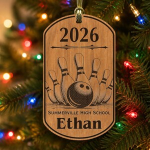 May include: A rectangular wooden ornament with rounded corners featuring a laser-engraved bowling design. The text 2026 is at the top, followed by a bowling ball and pins, with Summerville High School and the name Ethan engraved below.
