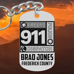 May include: Silver keyring with a black and white design. It says "FIRE/EMS POLICE 911 DISPATCH BRAD JONES FREDERICK COUNTY".