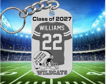 May include: A silver-toned metal keychain tag featuring the text Class of 2027, WILLIAMS, 22, and WILDCATS. The design includes a graphic of a jersey and a football helmet with the text Success isn't given. It's earned. printed on it.