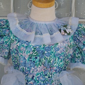 May include: A light blue dress with a floral print and a large, ruffled collar. The dress has short sleeves and a white lace trim.