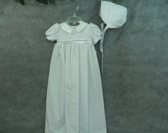 May include: A white christening gown with a satin ribbon and lace trim, and a matching white bonnet.