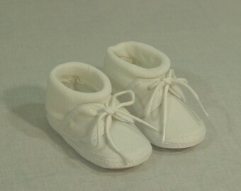 May include: A pair of white baby booties with lace-up closures. The booties have a soft, knitted cuff.
