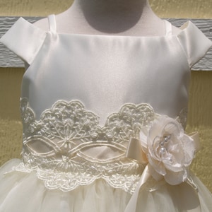 Puede incluir: Un vestido de satén blanco con un corpiño de encaje y una falda de tul. El vestido tiene un adorno de flores en la cintura.