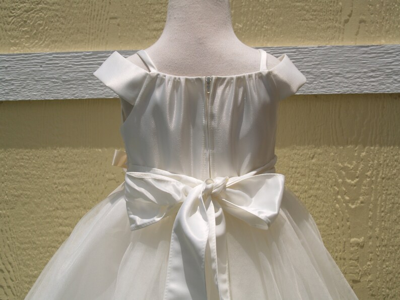 May include: White off-the-shoulder tulle dress with a satin bodice and a large satin bow at the back.
