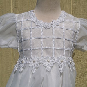 May include: White tulle dress with a grid pattern and pearl accents. The dress has puff sleeves and a lace trim around the neckline and hem.
