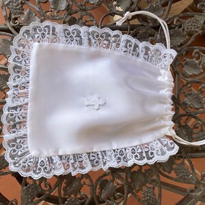 May include: White satin drawstring bag with a lace trim and a small embroidered cross. The bag is perfect for holding small items like jewelry or keepsakes.