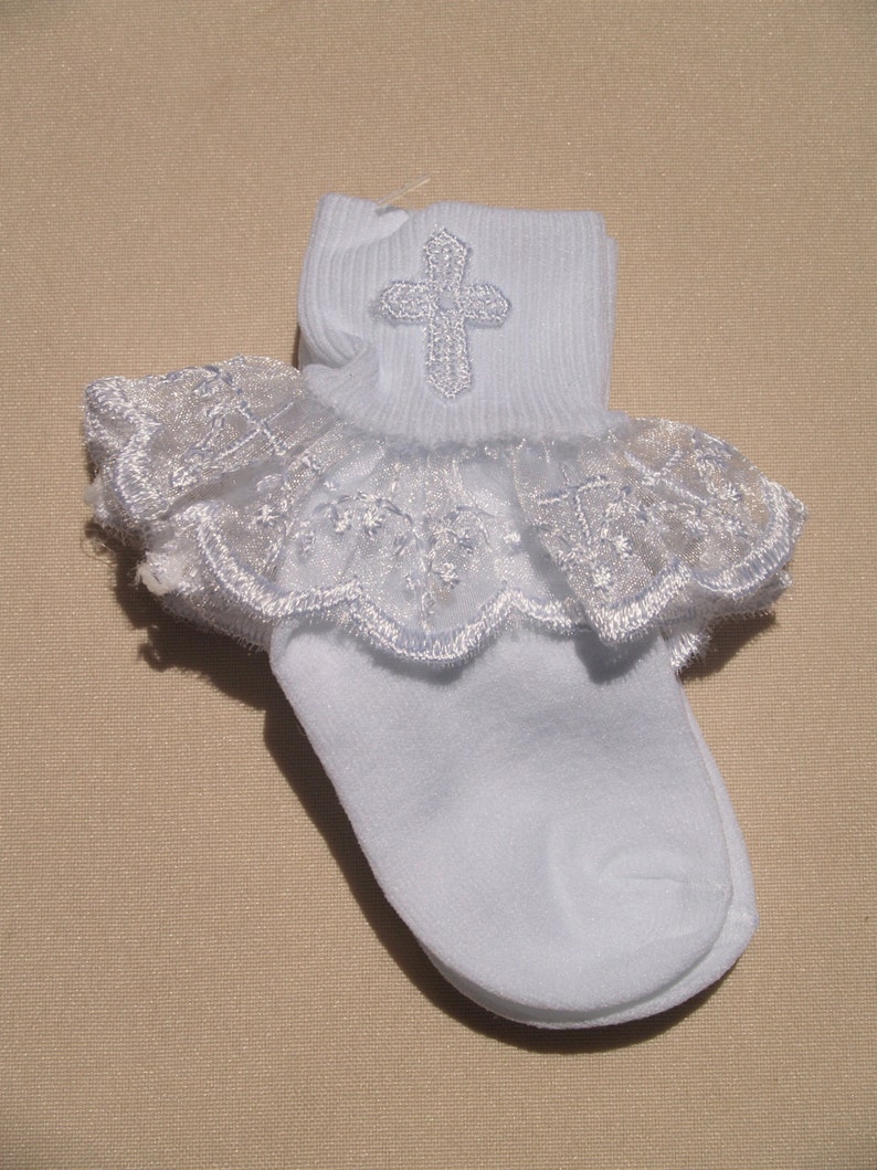 May include: White lace baby socks with a silver cross embroidered on the top of the sock.