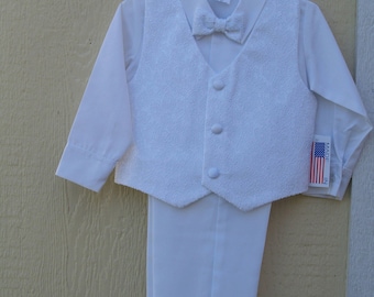 May include: A white formal suit for a child, including a long-sleeved shirt, textured vest with three buttons, matching pants, and a bow tie. The suit is hanging on a white hanger. A tag with the American flag is attached.