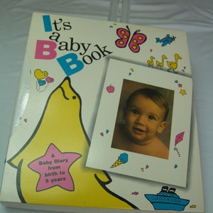 May include: A yellow and pink baby book with the text "It's a Baby Book" and a picture of a baby. The book is a baby diary from birth to 5 years.