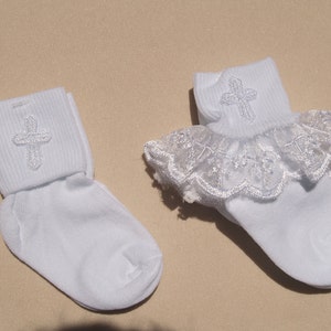 May include: Two pairs of white socks with a silver embroidered cross on the cuff. One pair has a white lace ruffle around the top.