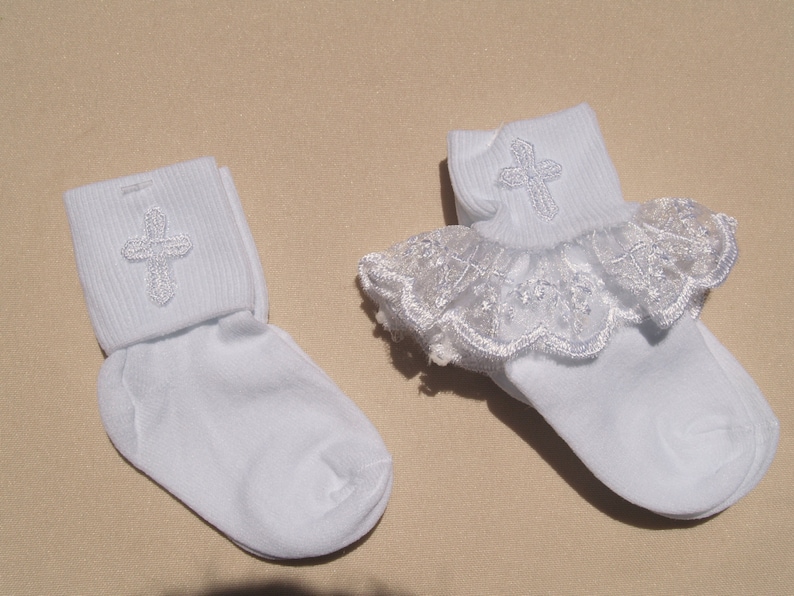 May include: Two pairs of white socks with a silver embroidered cross on the cuff. One pair has a white lace ruffle around the top.