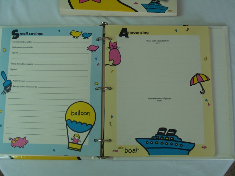 May include: A yellow binder with a blue and white boat on the cover. The binder has a section for "small savings" with a place to record savings bond information. The other side of the binder has a section for "announcing" with a place to put birth announcements and newspaper clippings.