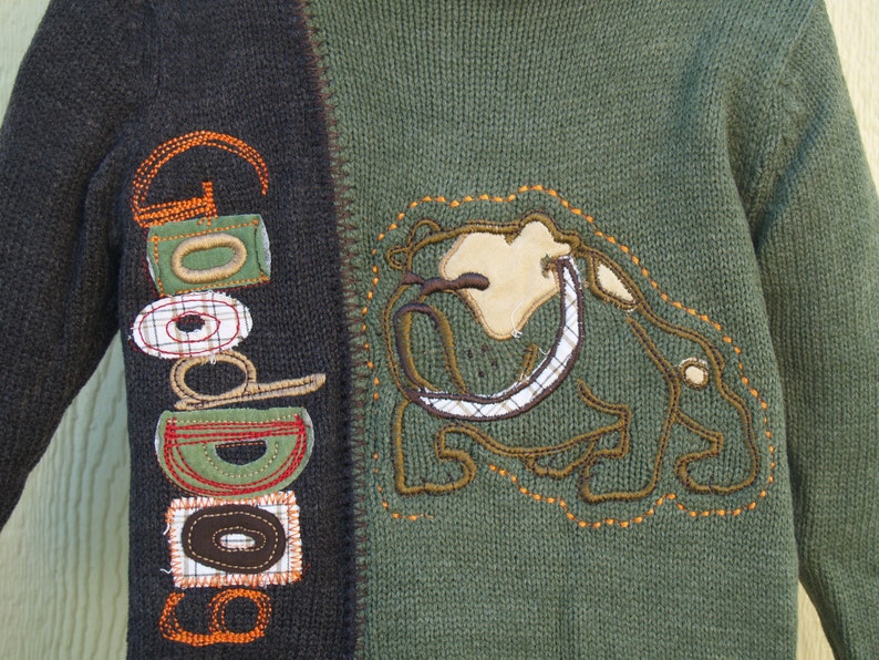May include: A green and brown sweater with a brown and white embroidered bulldog on the front. The sweater has the word "Good" embroidered on the left sleeve.