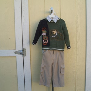 May include: A green and black sweater with a brown and white embroidered design. The sweater has a white collared shirt underneath. The sweater is paired with beige cargo pants.
