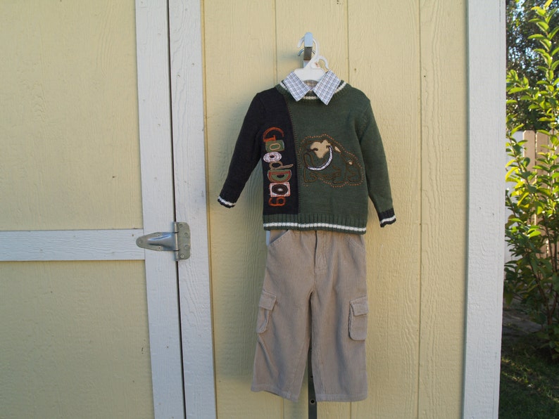 May include: A green and black sweater with a brown and white embroidered design. The sweater has a white collared shirt underneath. The sweater is paired with beige cargo pants.