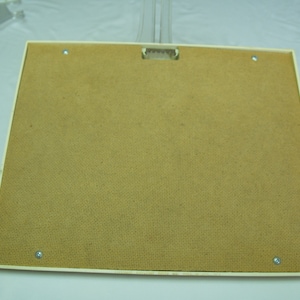 May include: The back of a white picture frame with a brown cardboard backing. The frame has four small silver screws holding the backing in place.