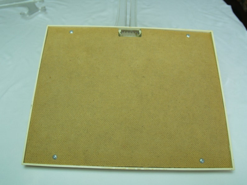 May include: The back of a white picture frame with a brown cardboard backing. The frame has four small silver screws holding the backing in place.