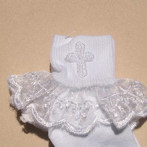 May include: White baby socks with a lace trim and a silver cross embroidered on the top of the sock.