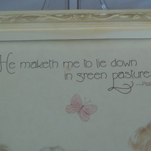 May include: A framed print with a white background and a quote from Psalm 23:2, "He maketh me to lie down in green pastures..." The quote is written in a cursive font. A small butterfly is drawn in the bottom right corner of the print.