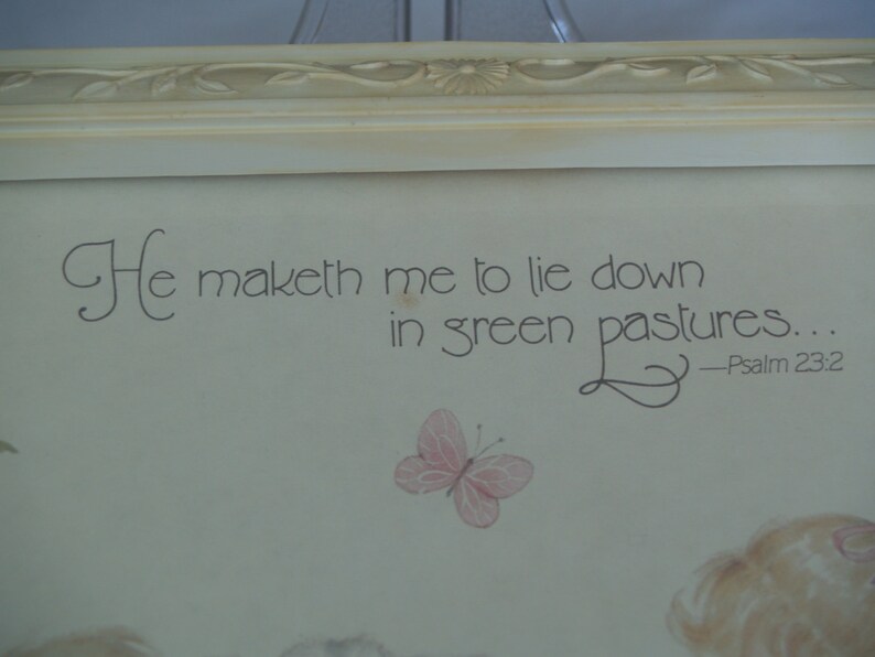 May include: A framed print with a white background and a quote from Psalm 23:2, "He maketh me to lie down in green pastures..." The quote is written in a cursive font. A small butterfly is drawn in the bottom right corner of the print.
