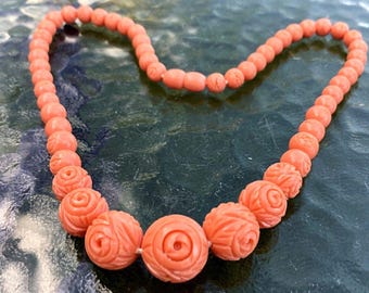 May include: A coral necklace with carved rose-shaped beads. The necklace is made of a light pink coral and is strung on a silver chain.
