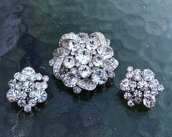 Può includere: Un set vintage di spilla e orecchini con strass. La spilla è un gruppo di strass trasparenti in una montatura argentata. Gli orecchini sono versioni più piccole e abbinate della spilla.