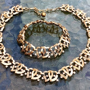 May include: A gold-tone necklace and bracelet set with a heart-shaped design and clear rhinestones.