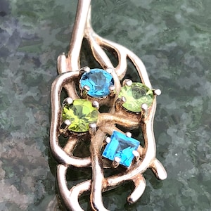 May include: A silver pendant with a leaf design featuring four gemstones: two blue and two green.