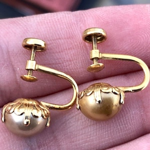 May include: A pair of gold tone clip-on earrings with a pearl-like center and a decorative design around the edge.