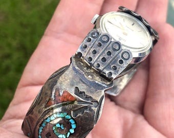 May include: A silver watch with a turquoise and red stone inlay on the band. The watch face is white with black hands and markers.